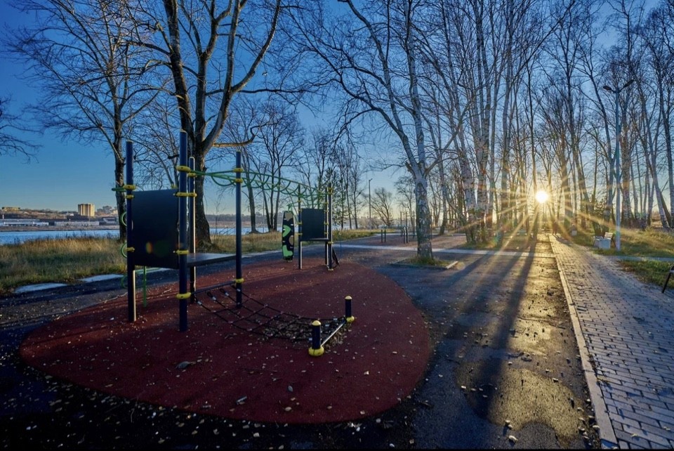 Small white house atop a grassy hill under a clear teal sky. A lone tree stands to the left. A person sits on the porch, evoking solitude and calm.