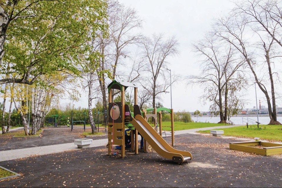 Modern arch-shaped building with glass facade reflects in an infinity pool at sunset. A silhouetted palm tree adds to the serene, elegant scene.
